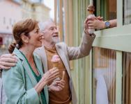 An older, likely retired couple, are shopping at a street-side ice cream stand. They're smiling while being handed a pink ice cream cone.