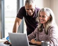 A middle-aged couple looking at a laptop on a desk at home.